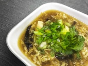 A close up of a bowl of hot and sour soup topped with green onions and cilantro.