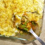 Vegetarian Shepherd's Pie in a casserole dish with a spoon filled with mushrooms, carrots, onions, celery, peas, and gravy.