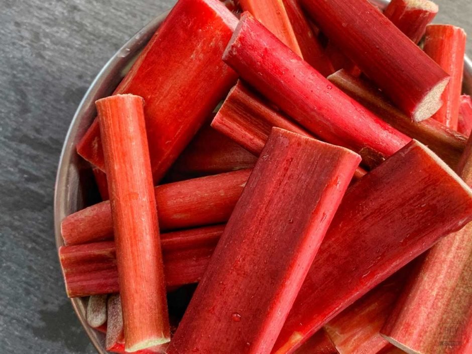 A metal bowl filled with cut red rhubarb stalks on a slate table.